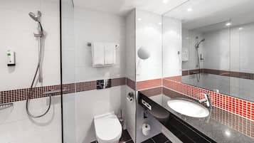 A modern bathroom with a glass shower enclosure, a white toilet, a sink with a black countertop, and red-tiled accents.