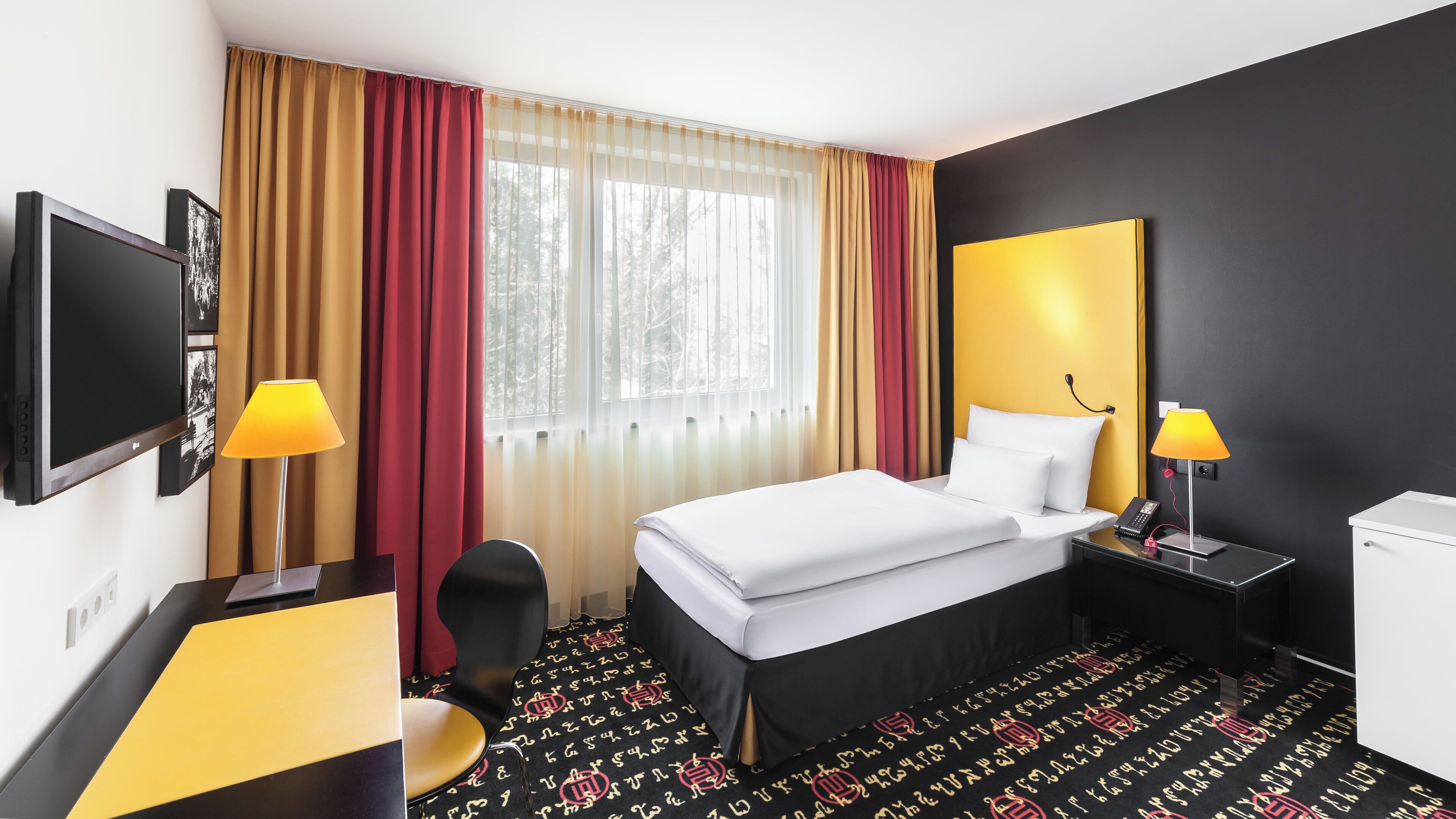 Ein Hotelzimmer mit einem Bett, Nachttischlampen, einem Schreibtisch mit Stuhl, einem Fernseher und einem Fenster mit Vorhängen.