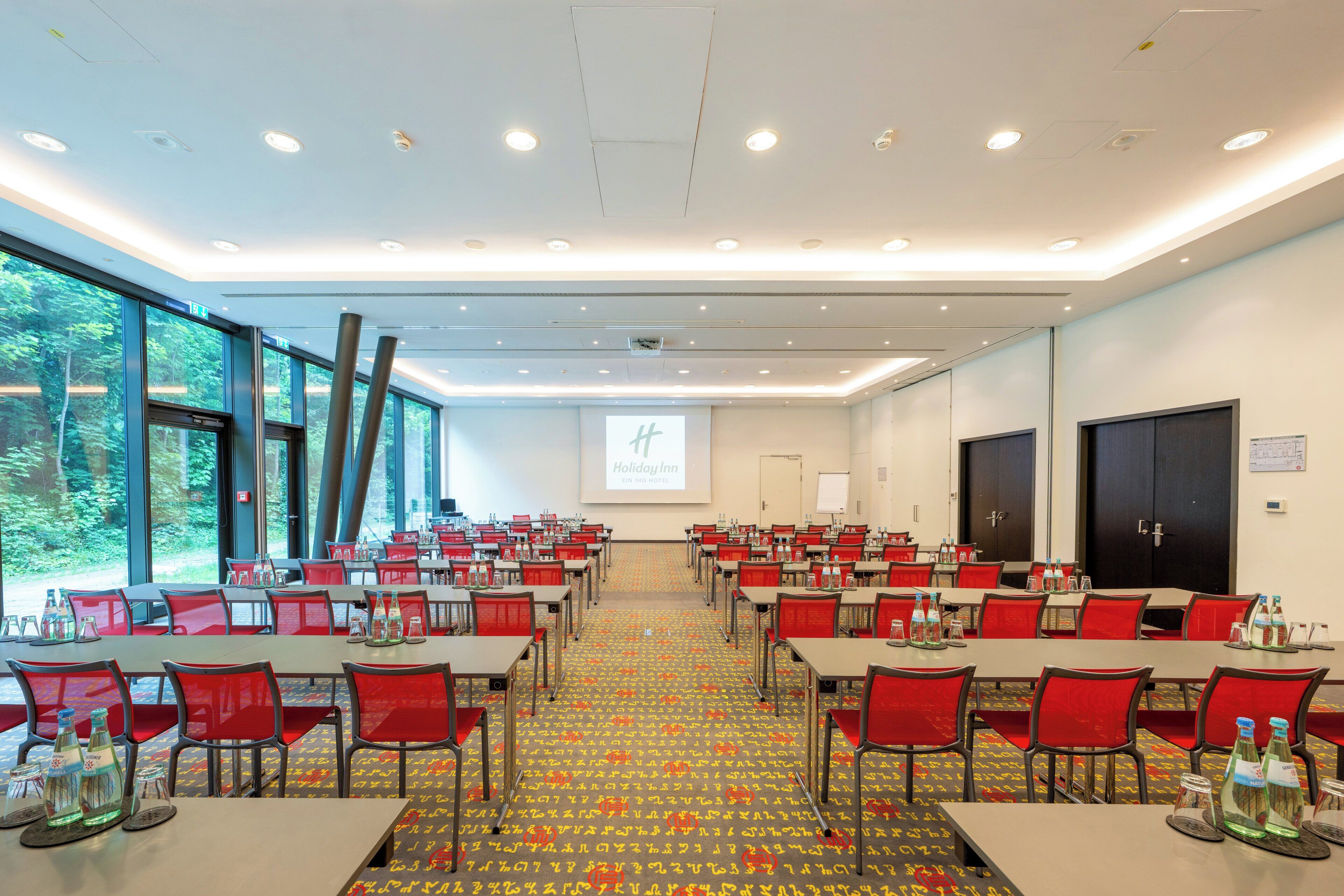 Ein Konferenzraum mit Tischen, Stühlen, großen Fenstern und einer Projektionsleinwand.