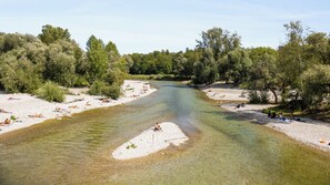 A river with clear water surrounded by trees and a sandy beach with people sunbathing. - Holiday Inn Munich- Westpark by IHG (Munich)