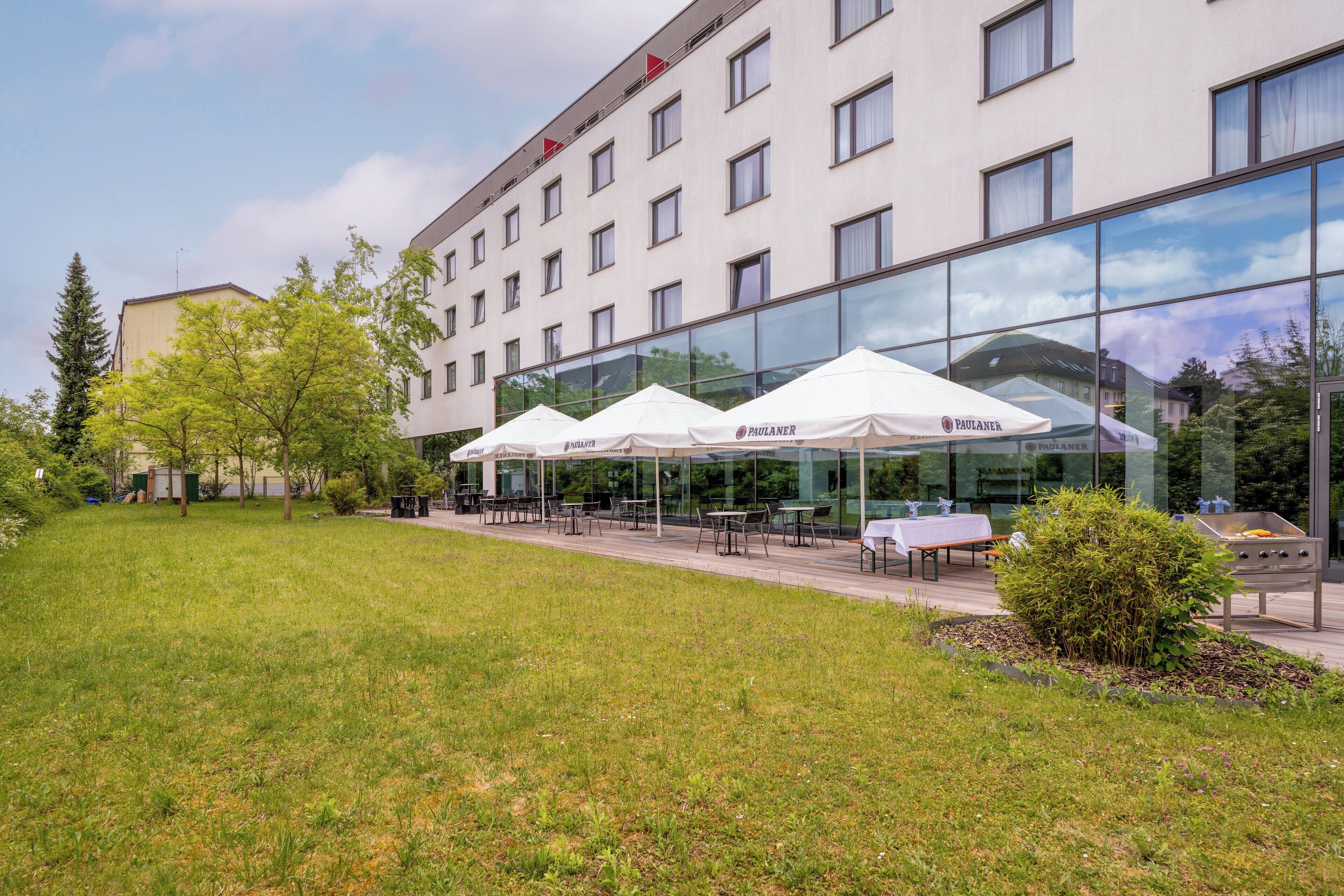 A hotel with outdoor seating, a grassy area, and a modern glass facade.