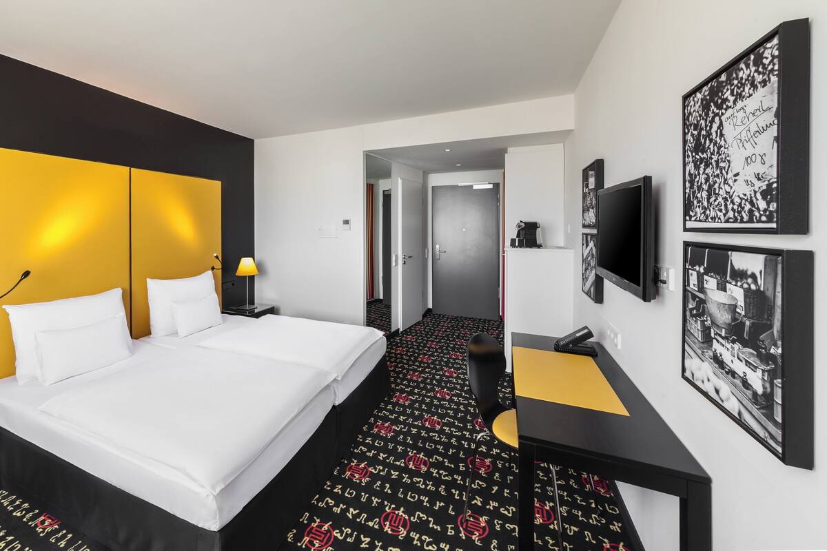 A hotel room with a large bed, bedside tables with lamps, a desk, and a TV.