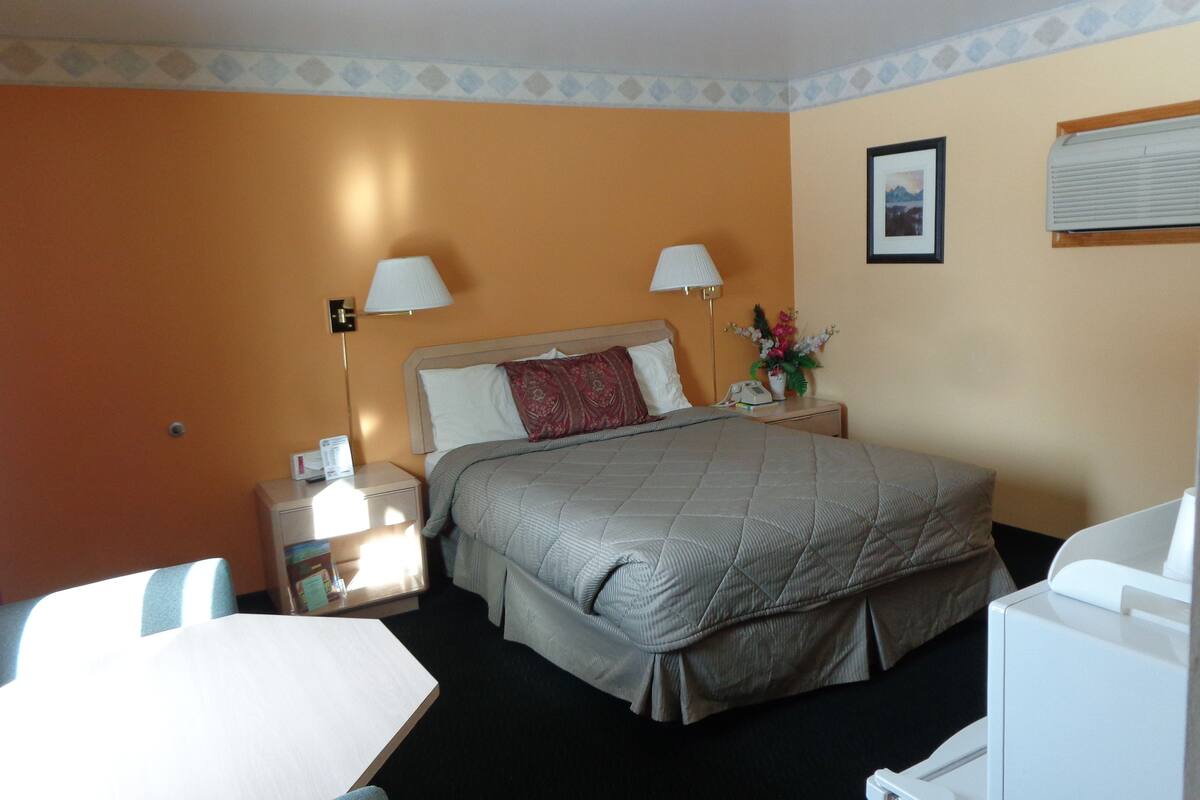 Una camera d'albergo con un letto, lampade sui comodini, una scrivania e una sedia.