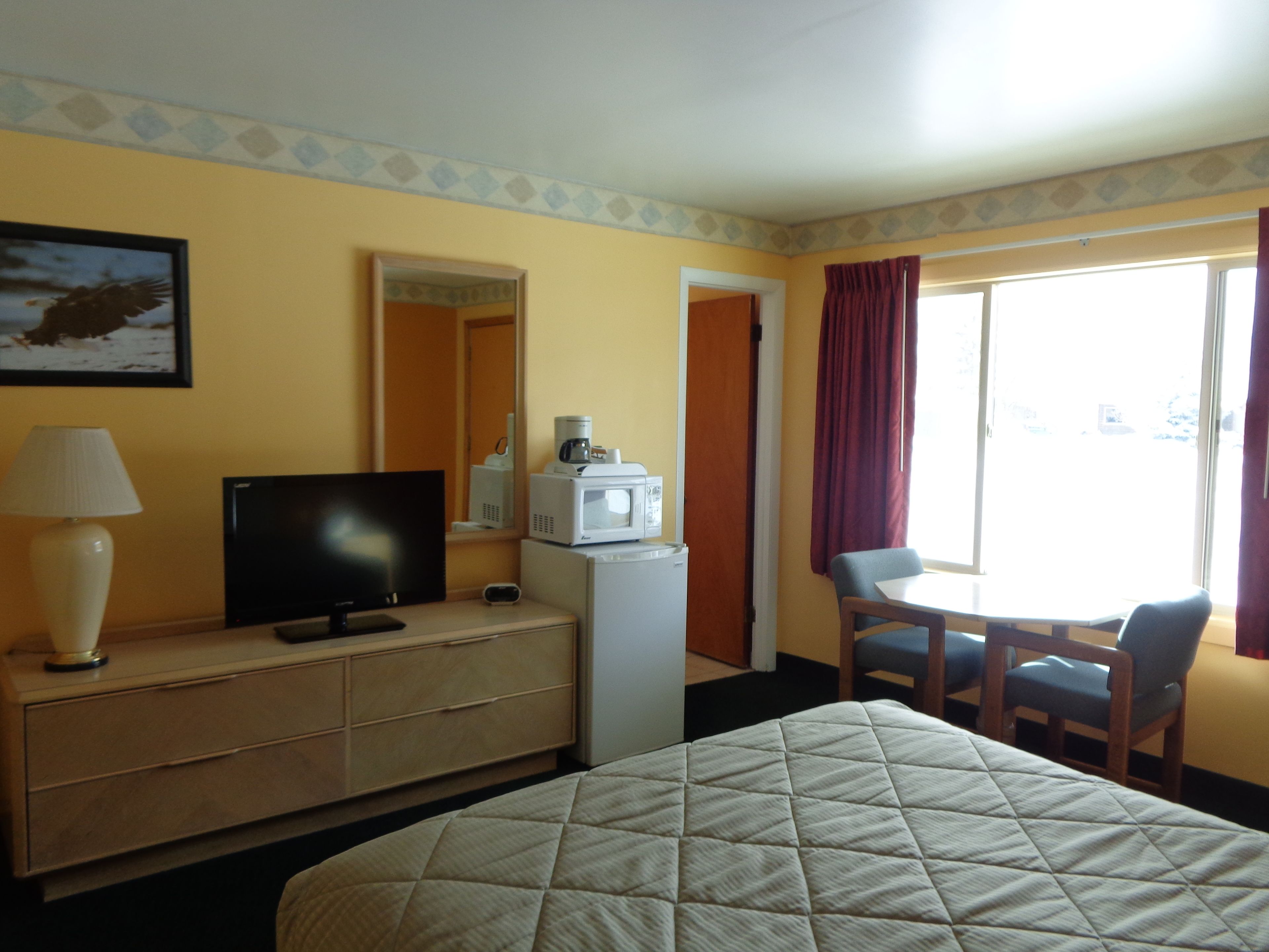 Une chambre d’hôtel équipée d’un lit, d’une télévision posée sur une commode, d’un four à micro-ondes, d’une machine à café et d’un coin repas avec une table et des chaises.