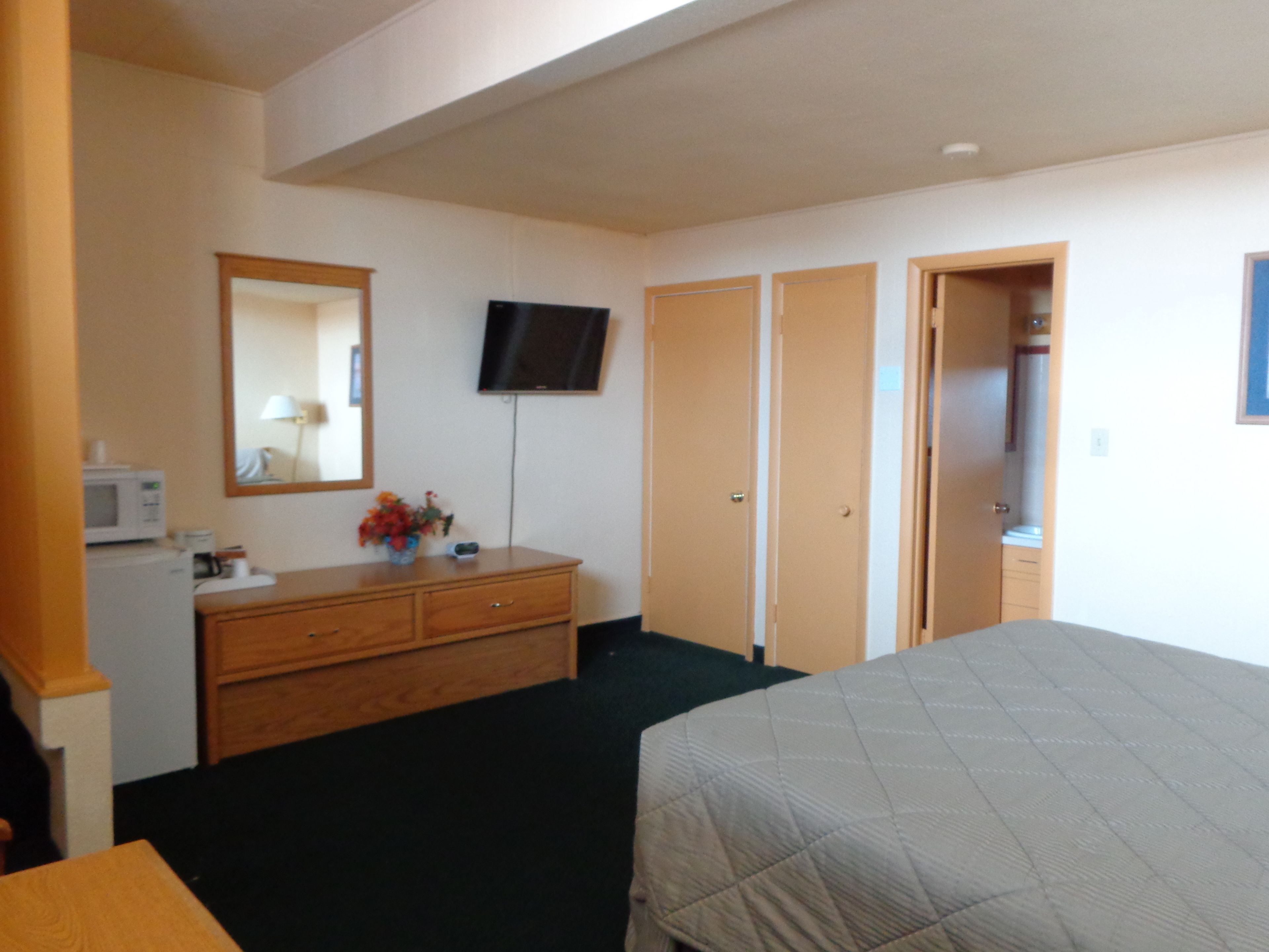 A hotel room with a bed, a dresser, a television, and a mirror.