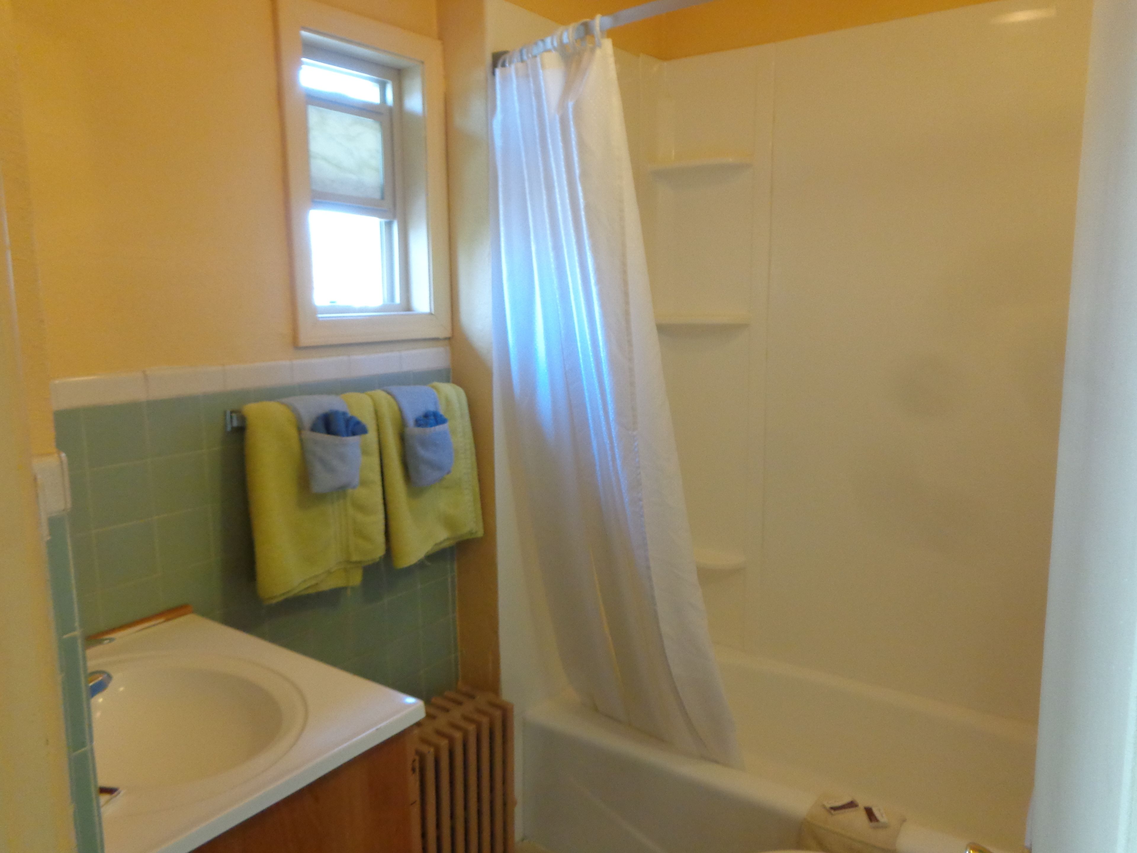 Een badkamer met een witte badkuip, een raam boven de wastafel en twee handdoeken aan de muur.