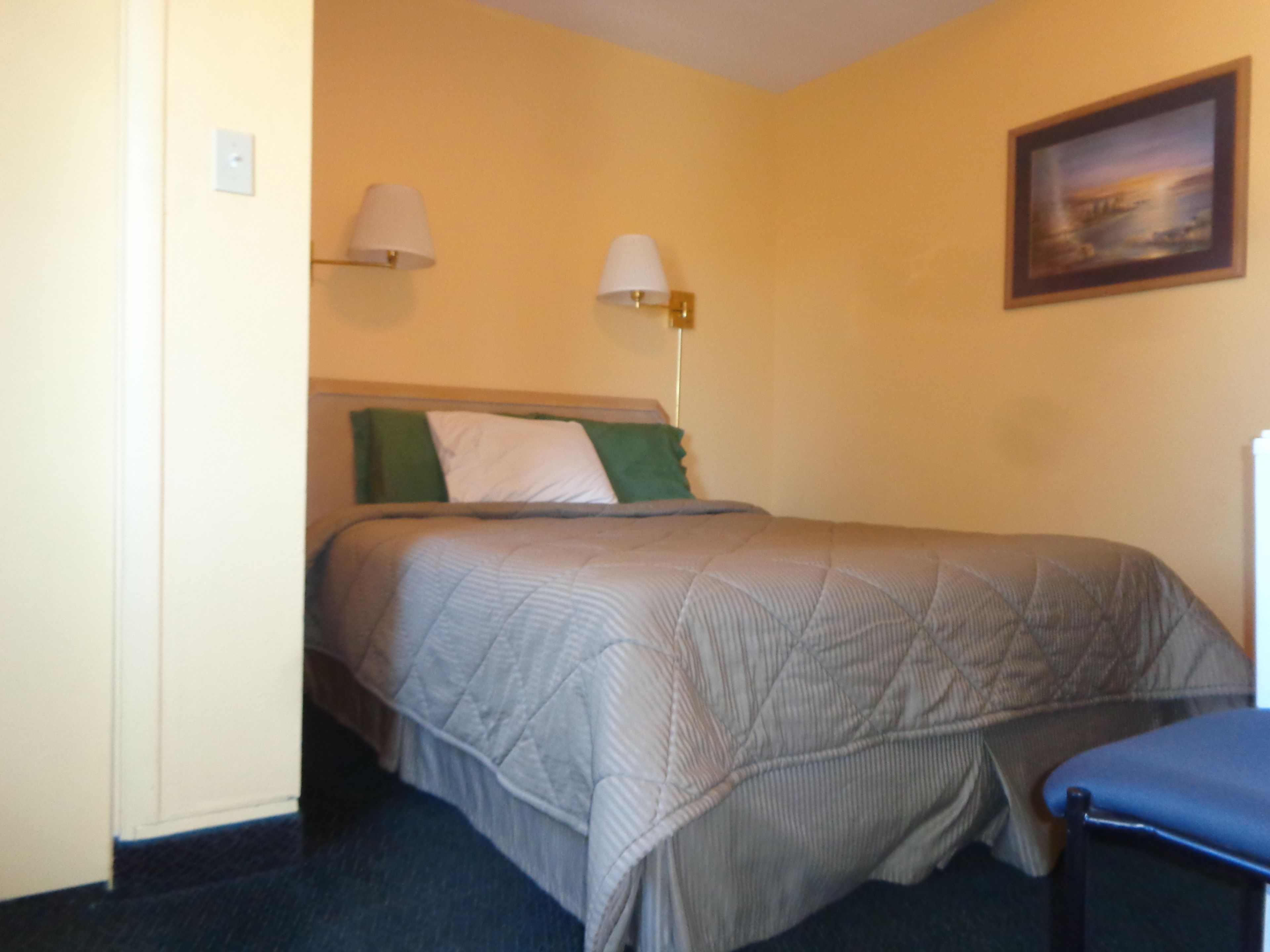 A hotel room with a bed, two bedside lamps, a painting on the wall, and a blue chair.