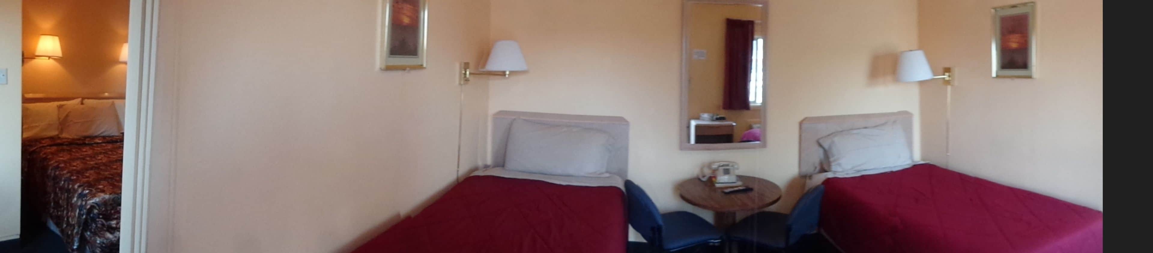 A hotel room with two single beds, a small round table, a chair, a mirror, and a door leading to another room.
