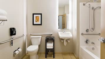 Un baño con inodoro, lavamanos y bañera. Hay un cuadro en la pared, un teléfono y un perchero para toallas.