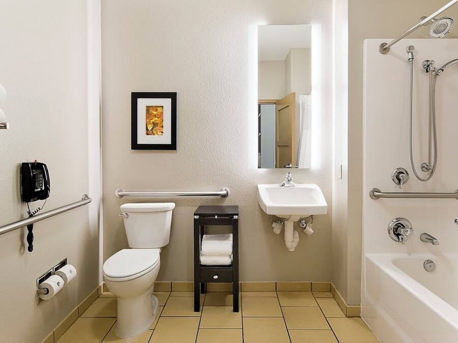 Un baño con inodoro, lavamanos y bañera. Hay un cuadro en la pared, un teléfono y un perchero para toallas.