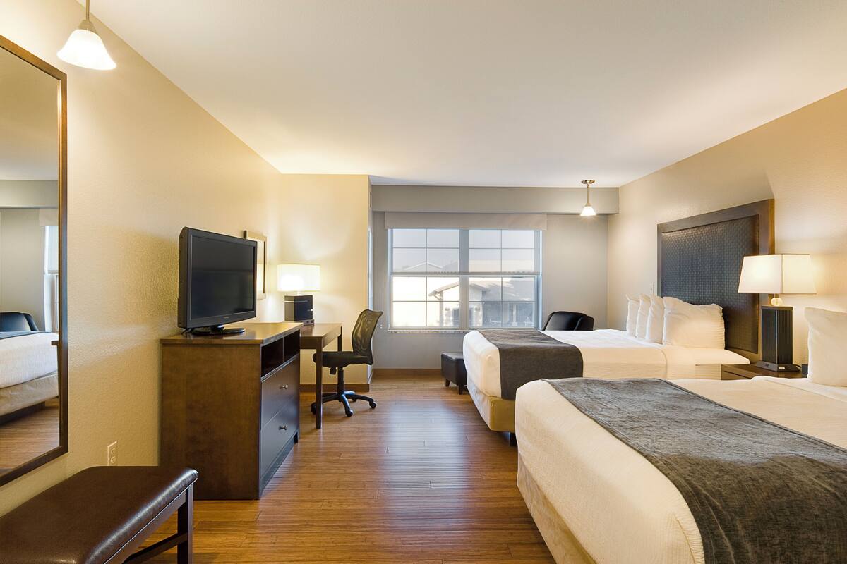 Ein Hotelzimmer mit Schreibtisch, Fernseher, zwei Betten, einem Sessel und einem Fenster.