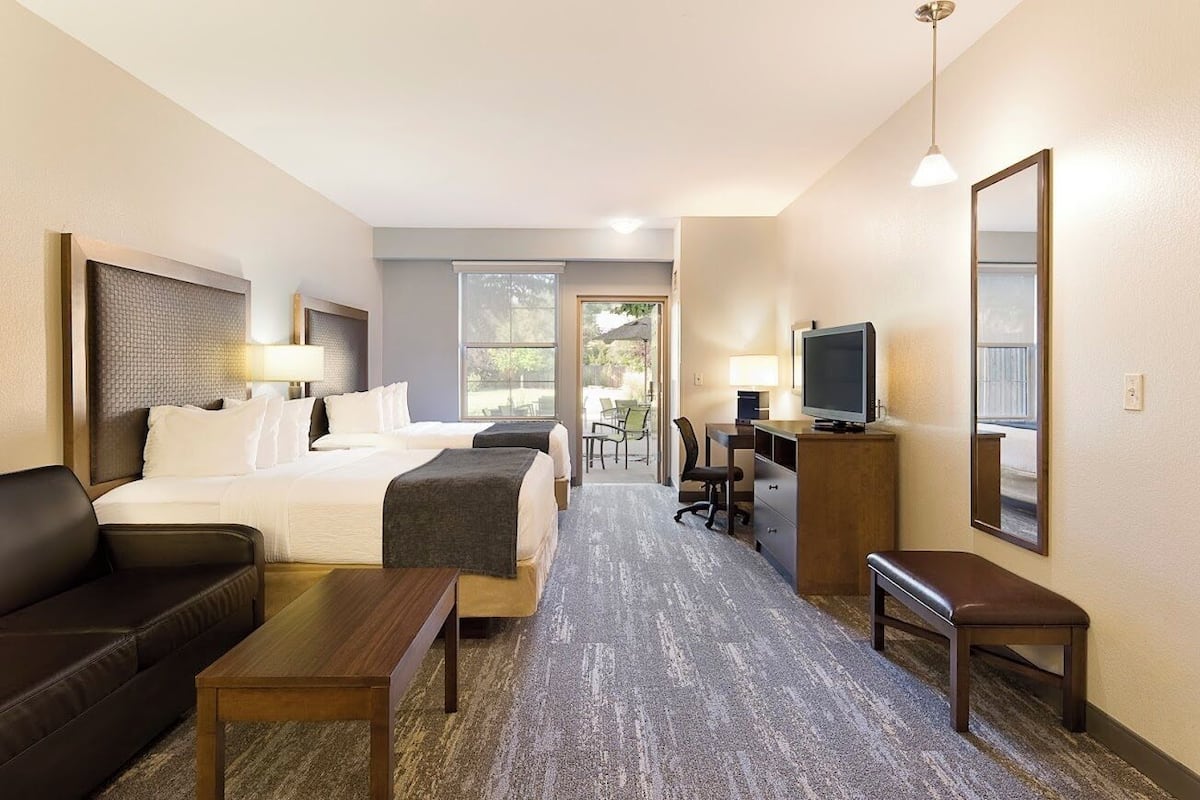 Ein Hotelzimmer mit Bett, Schreibtisch, Stuhl, Fernseher und einer Sitzbank.