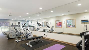 Uma academia com equipamentos de cardio, bancos de peso e colchonetes.