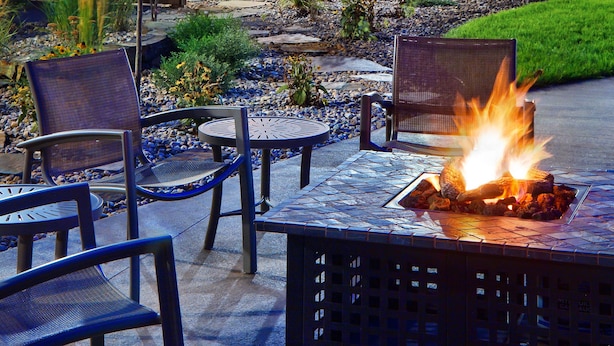 Un espacio al aire libre con asientos, una chimenea rodeada de sillas y una pequeña mesa.