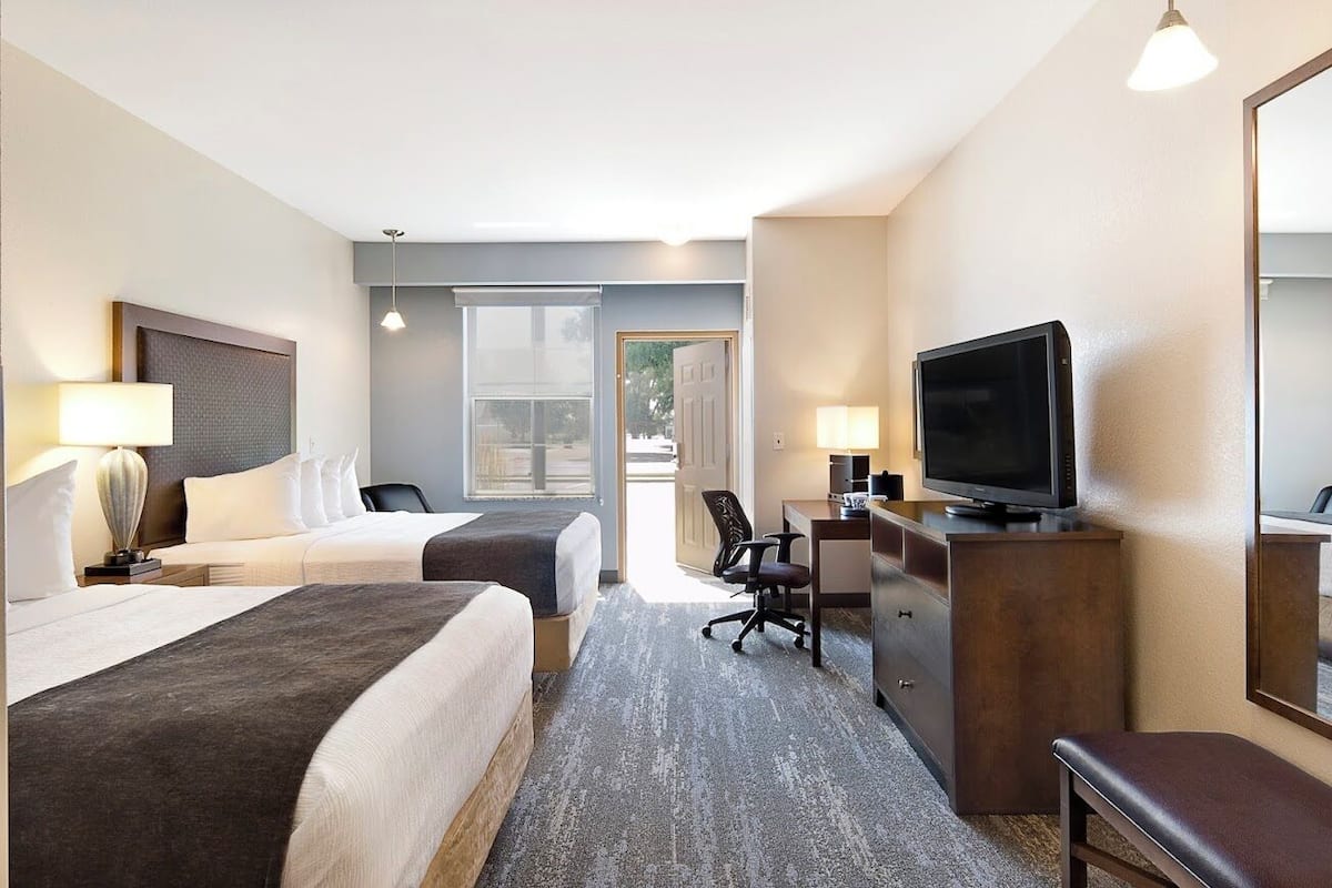 Ein Hotelzimmer mit zwei Betten, einem Schreibtisch, einem Fernseher und einem großen Fenster.