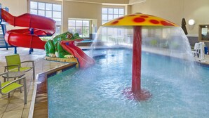 Una piscina interior con un tobogán con forma de rana y una fuente con forma de hongo.