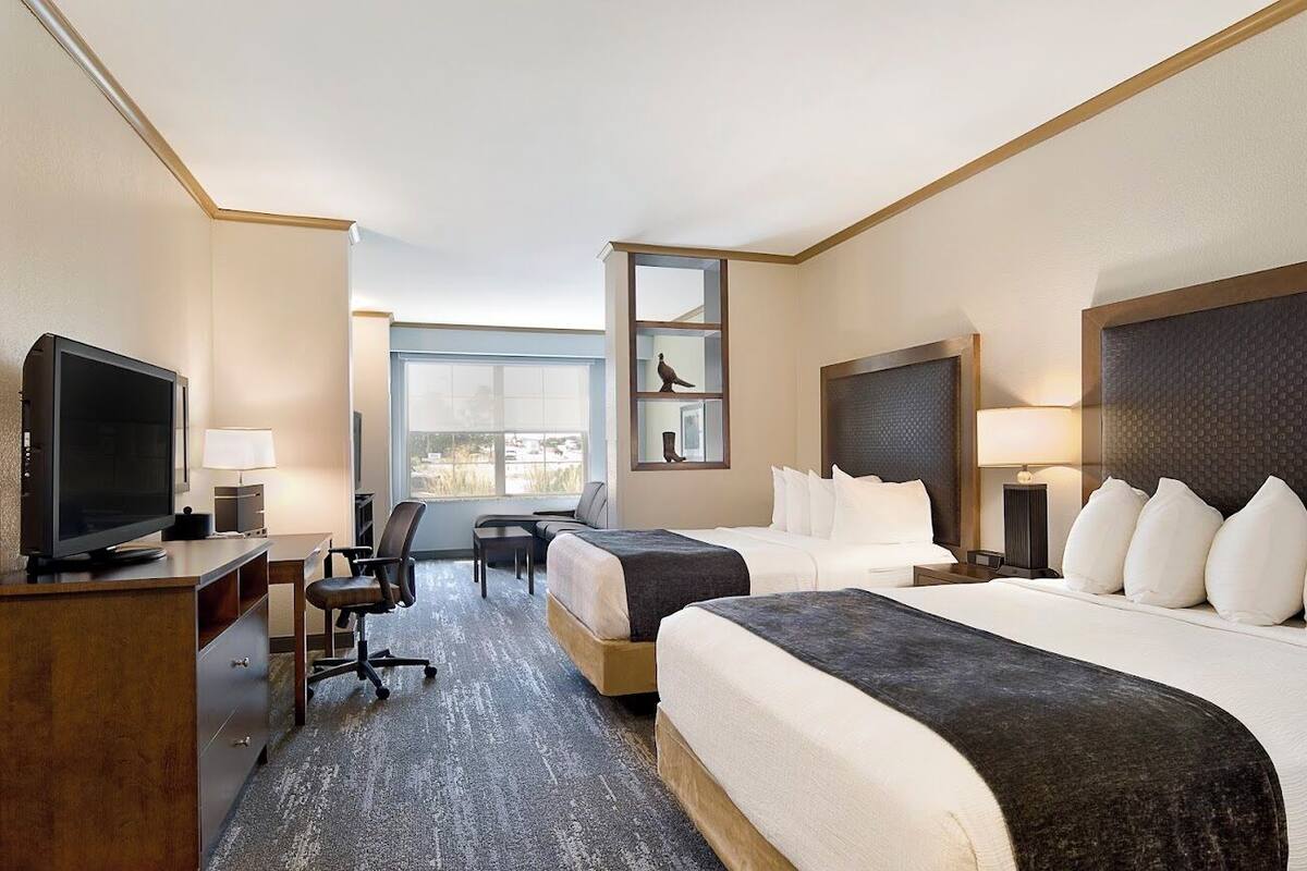Ein Hotelzimmer mit zwei Betten, einem Schreibtisch, einem Fernseher und einem großen Fenster.