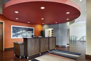A hotel reception area with a wooden reception desk, a large framed photograph on the wall, and a modern ceiling design.