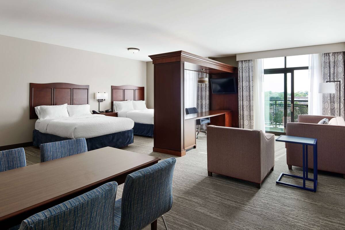 A hotel room with two beds, a desk, a chair, a sofa, and a TV.