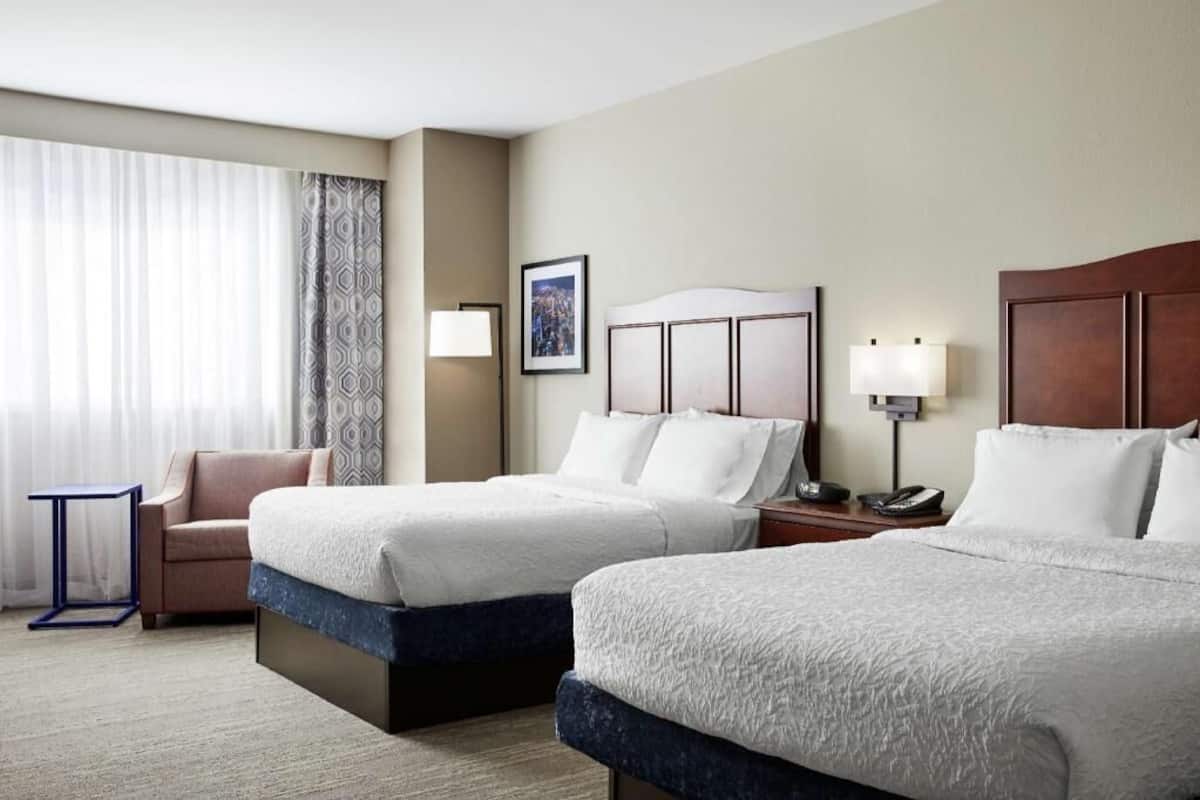 A hotel room with two beds, a chair, a small table, a lamp, and a picture on the wall.