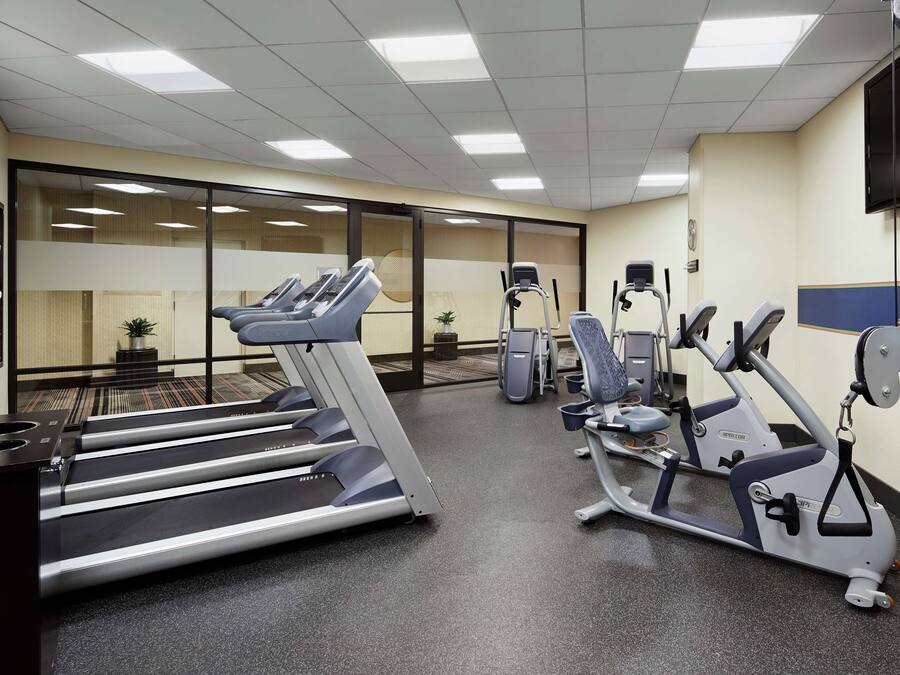 Et fitnesscenter med løbebånd, crosstrainere og et tv på væggen.