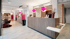 A modern reception area with a wooden reception desk, a seating area with chairs, and a visible kitchen in the background. - Best Western Hotel Brussels South (Sint-Pieters-Leeuw)