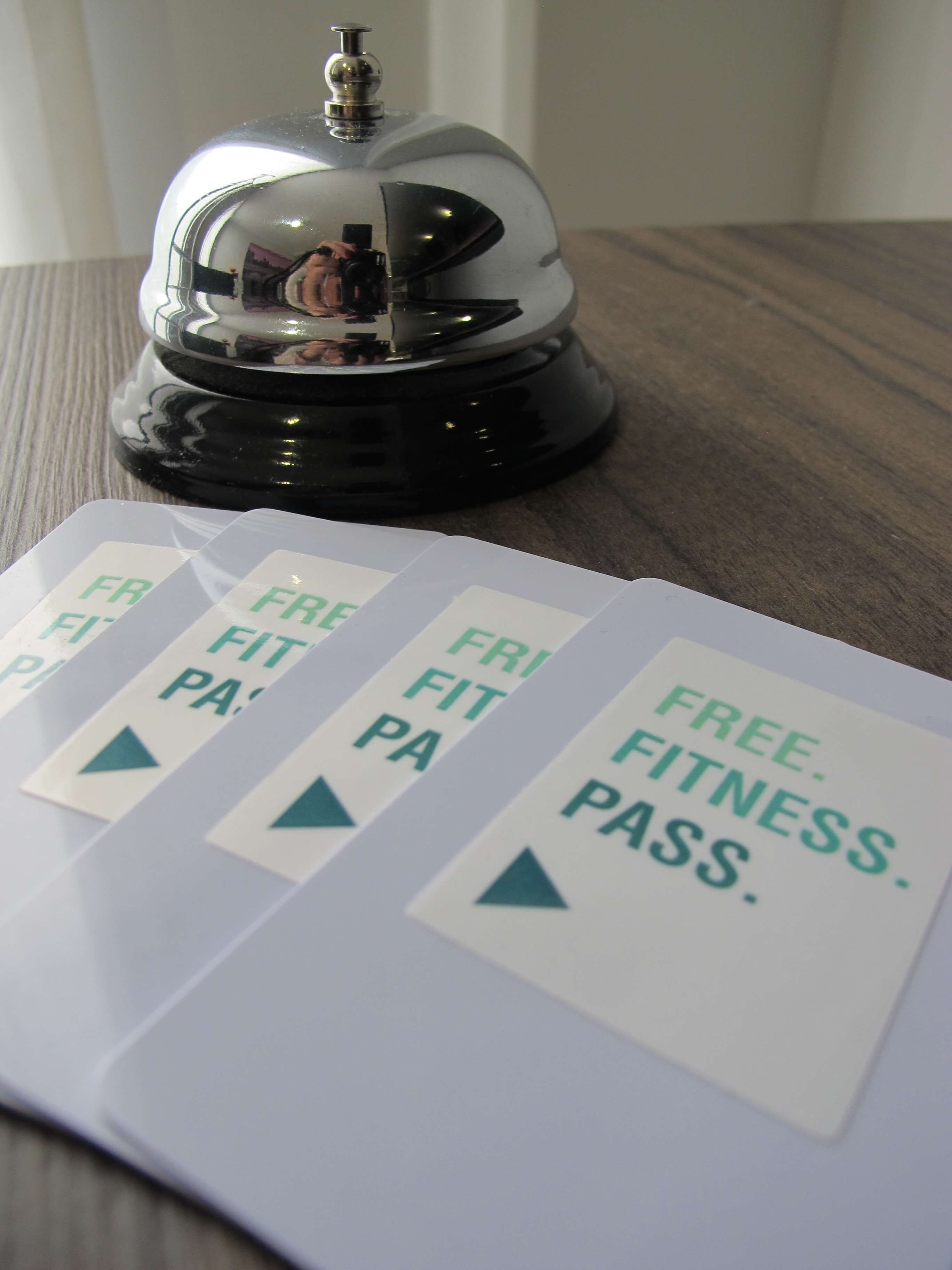 A hotel room with a wooden floor and a bell on a black base. There are signs on the floor indicating 'Free Fitness Pass'.