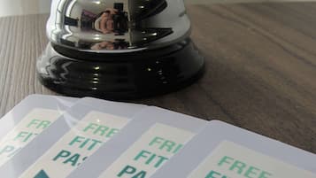 A hotel room with a wooden floor and a bell on a black base. There are signs on the floor indicating 'Free Fitness Pass'.