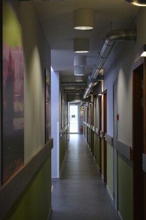 A long, narrow hallway with doors on both sides, a fire extinguisher on the right wall, and a ceiling vent running along the hallway.