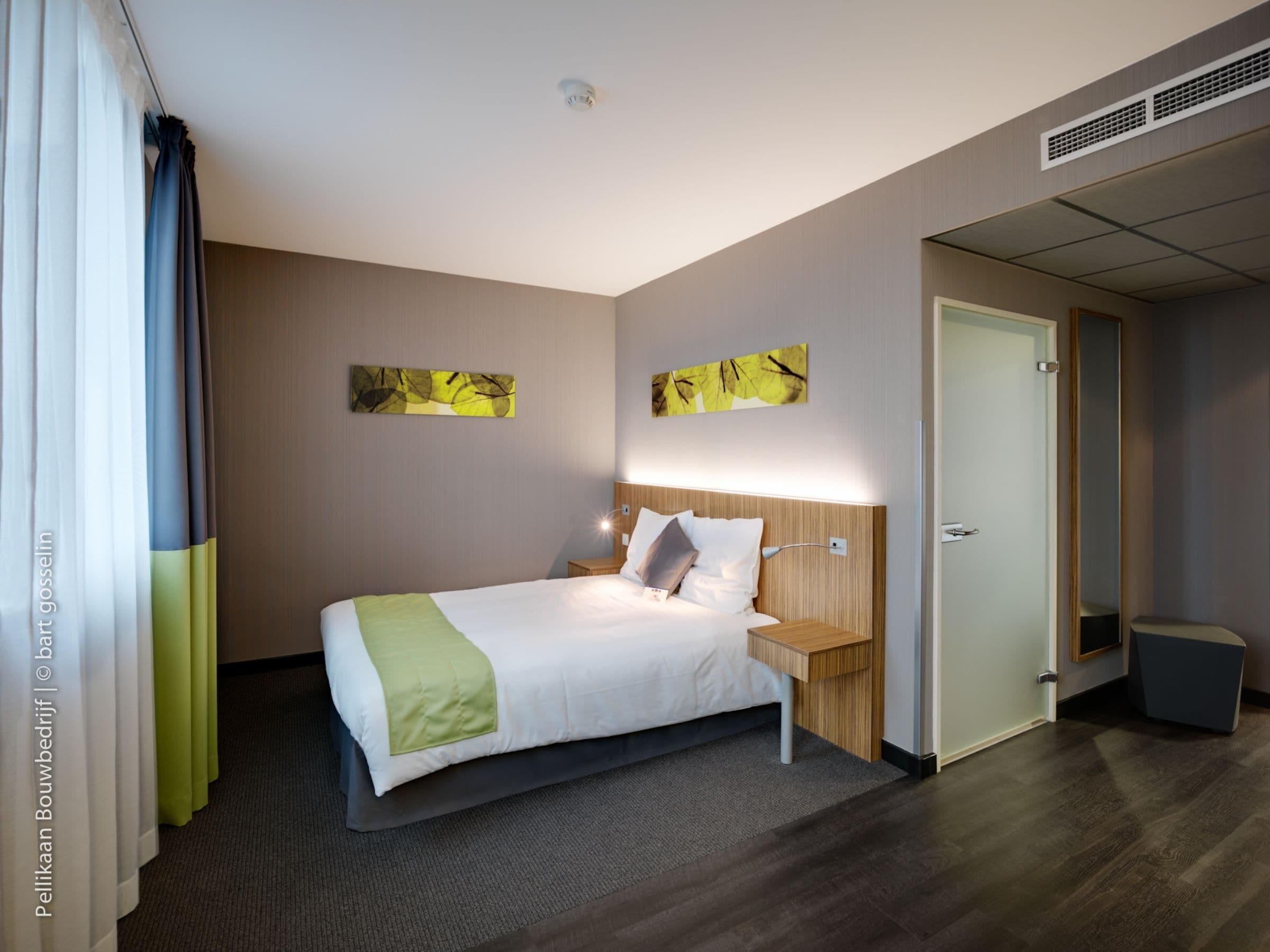 A hotel room with a large bed, a bedside table, a nightstand, a mirror, and a door.