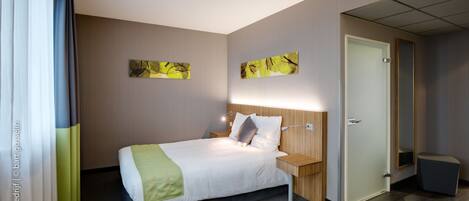 A hotel room with a large bed, a bedside table, a nightstand, a mirror, and a door.
