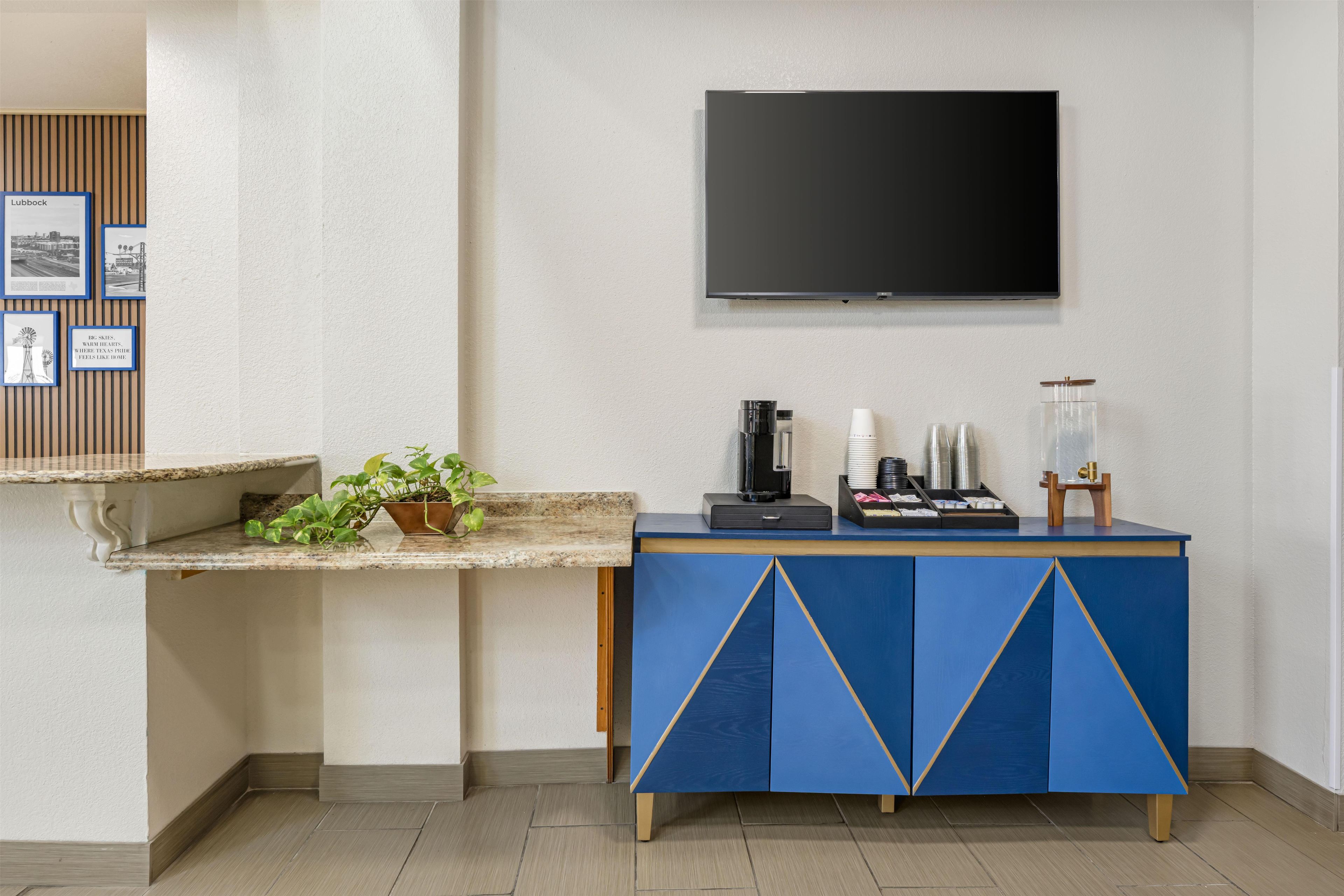 A hotel reception area with a flat-screen TV mounted on the wall, a coffee machine, and a plant on the counter.
