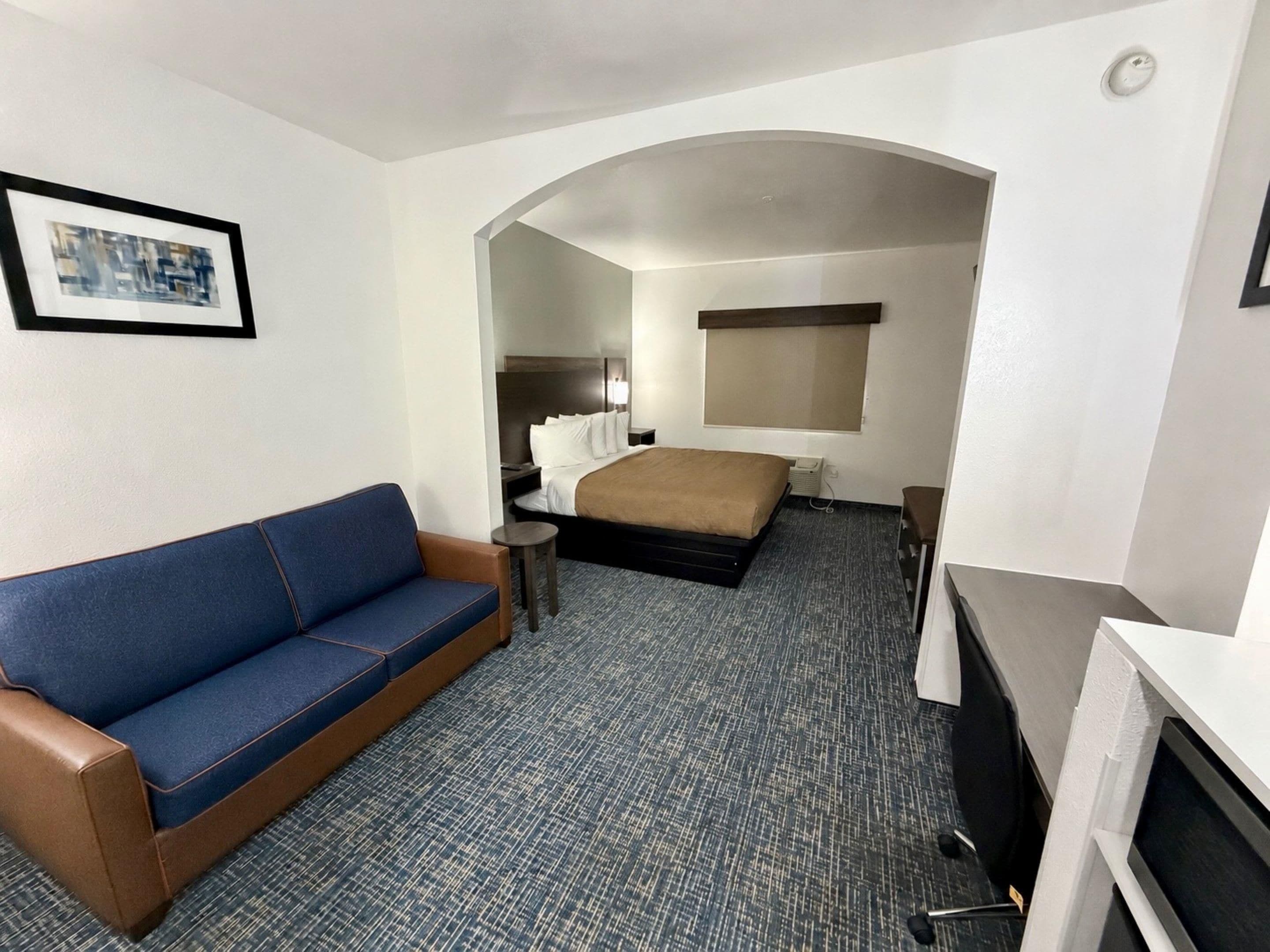 A hotel room with a sofa, a bed, a television, and a desk with a chair.