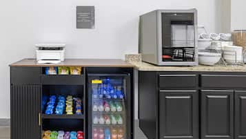 Una kitchenette con refrigerador lleno de bebidas, microondas y cafetera.