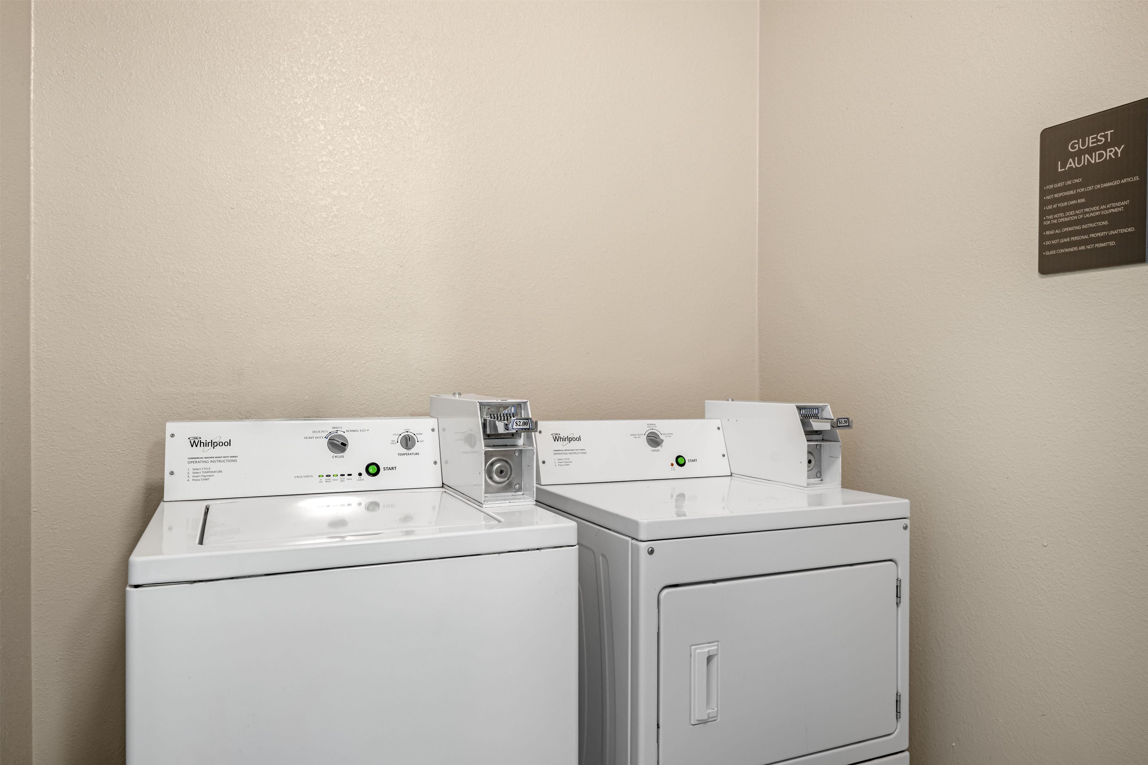 Un lavadero de hotel con dos lavadoras y secadoras Whirlpool, un letrero para huéspedes y las instrucciones de uso.
