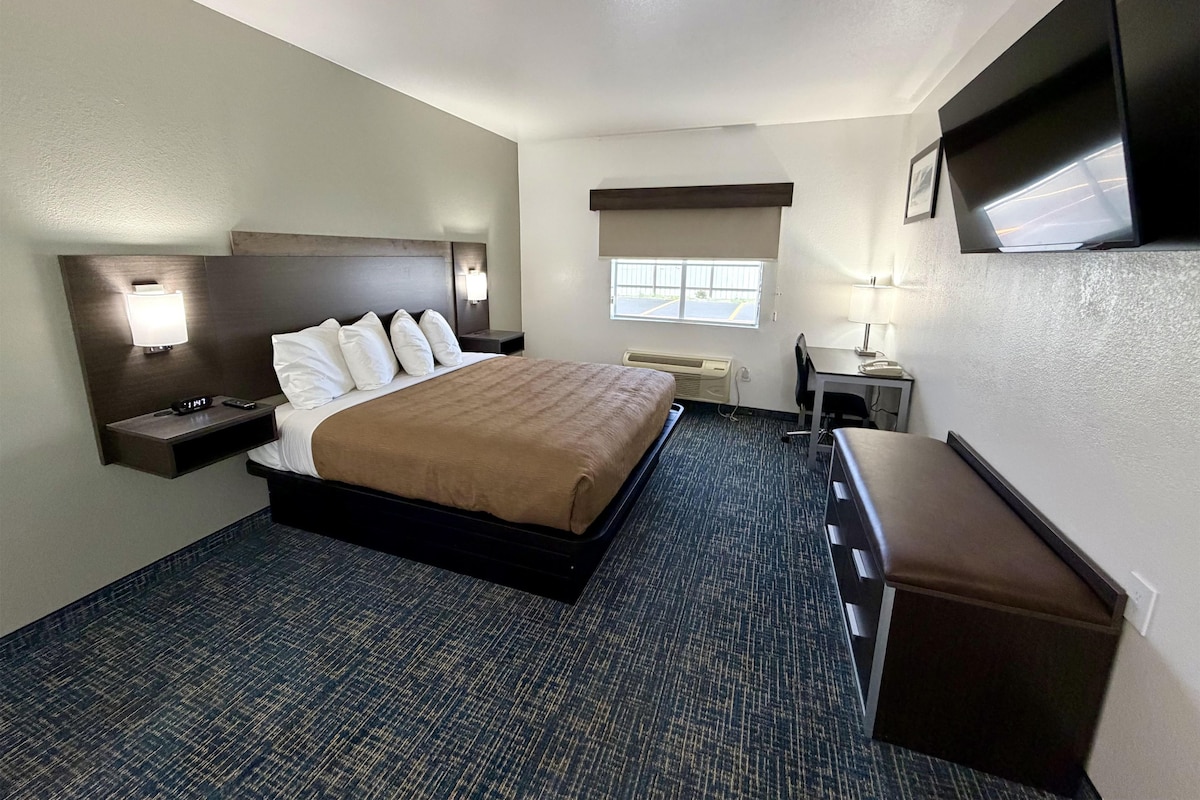 Habitación de hotel con cama, mesita de noche, lámpara, escritorio, silla y televisión de pantalla plana montada en la pared.
