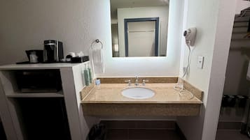 Un baño con lavamanos, espejo, toallero y una cafetera en la encimera.