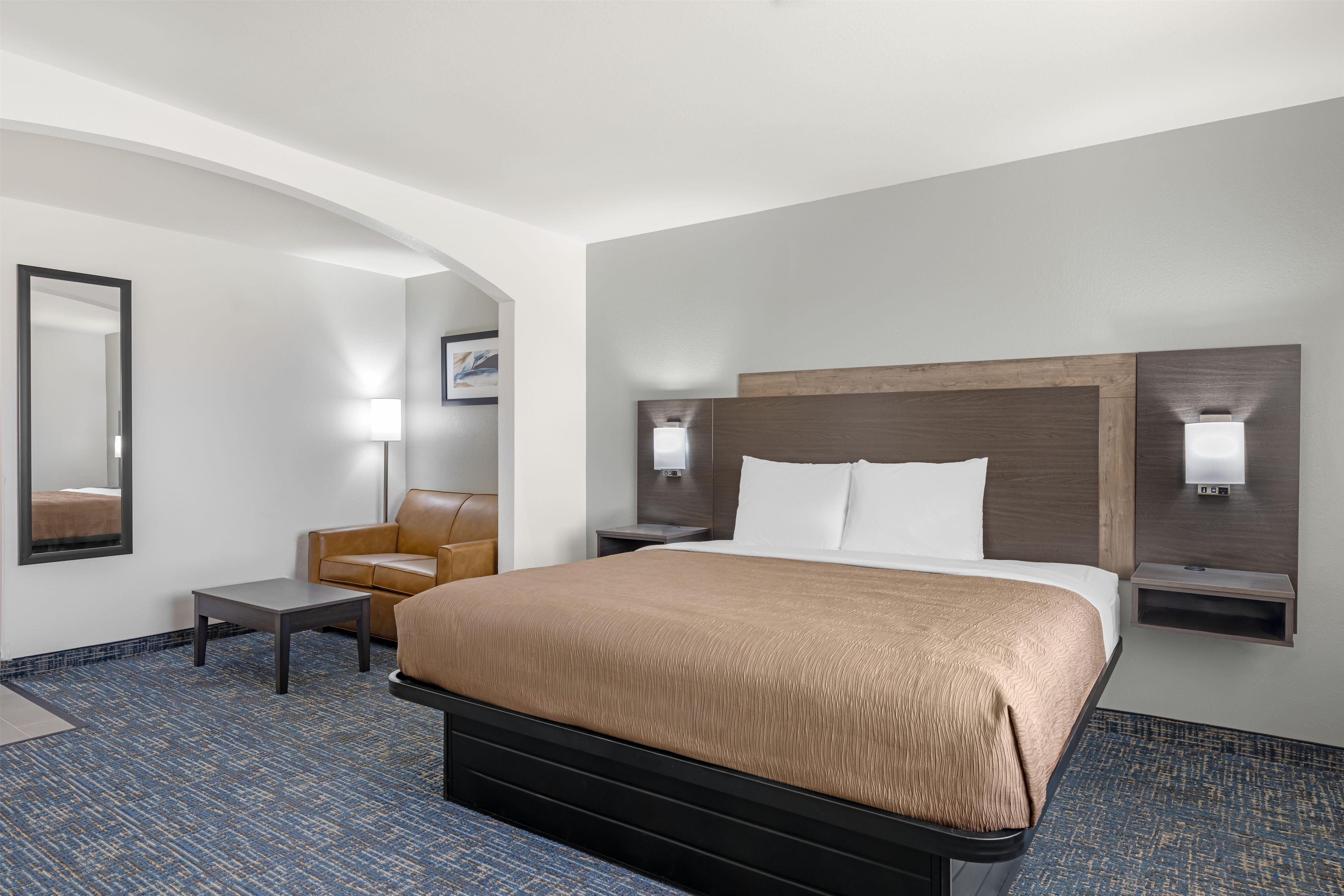 Una habitación de hotel con una cama, una silla, un escritorio y un espejo.