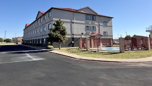 A multi-story building with a red roof, a gated parking area, and a clear sky.