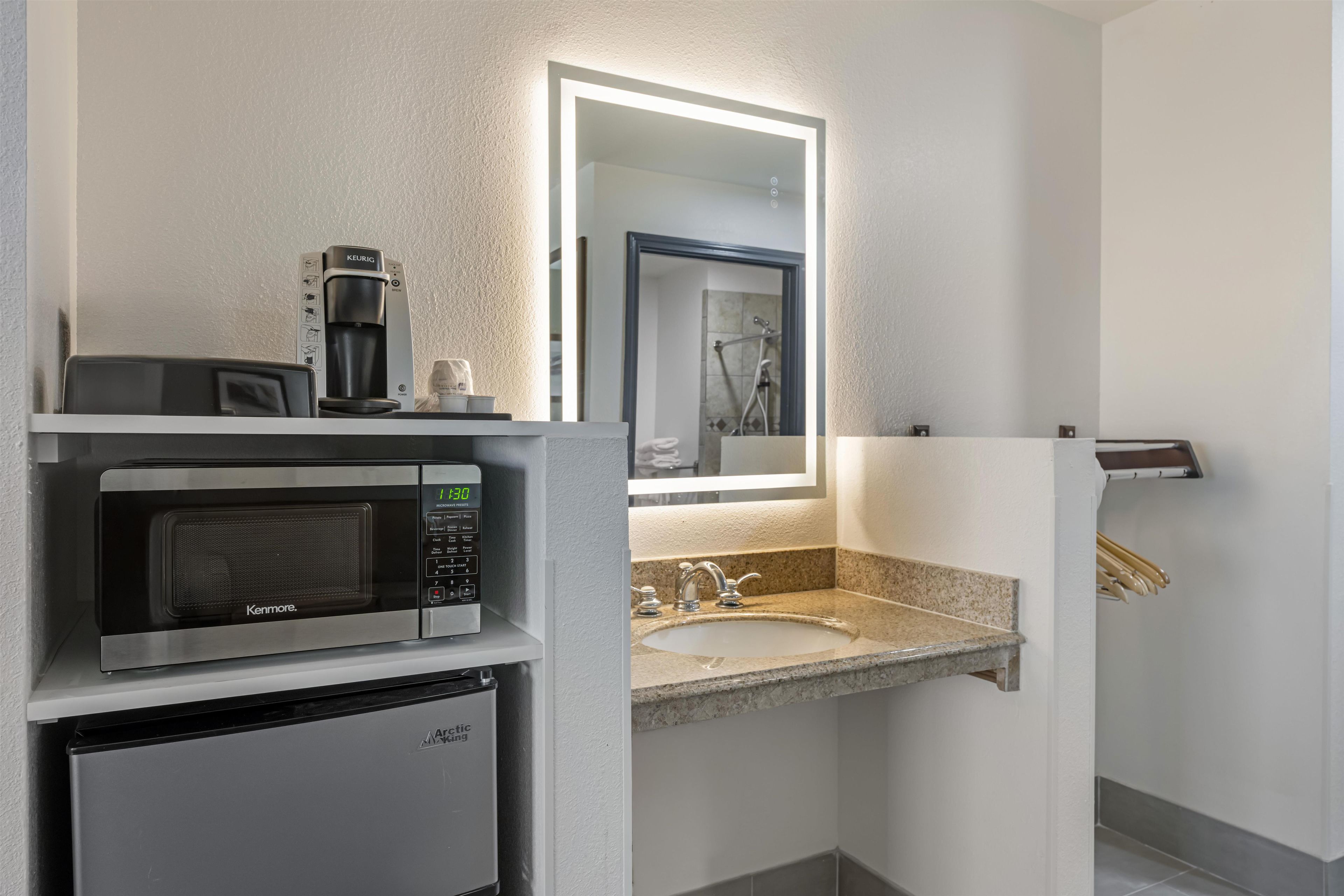 A compact hotel bathroom with a built-in coffee maker, microwave, and refrigerator.