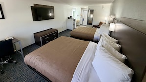 A hotel room with two beds, a desk, a television, and a bathroom visible in the background.
