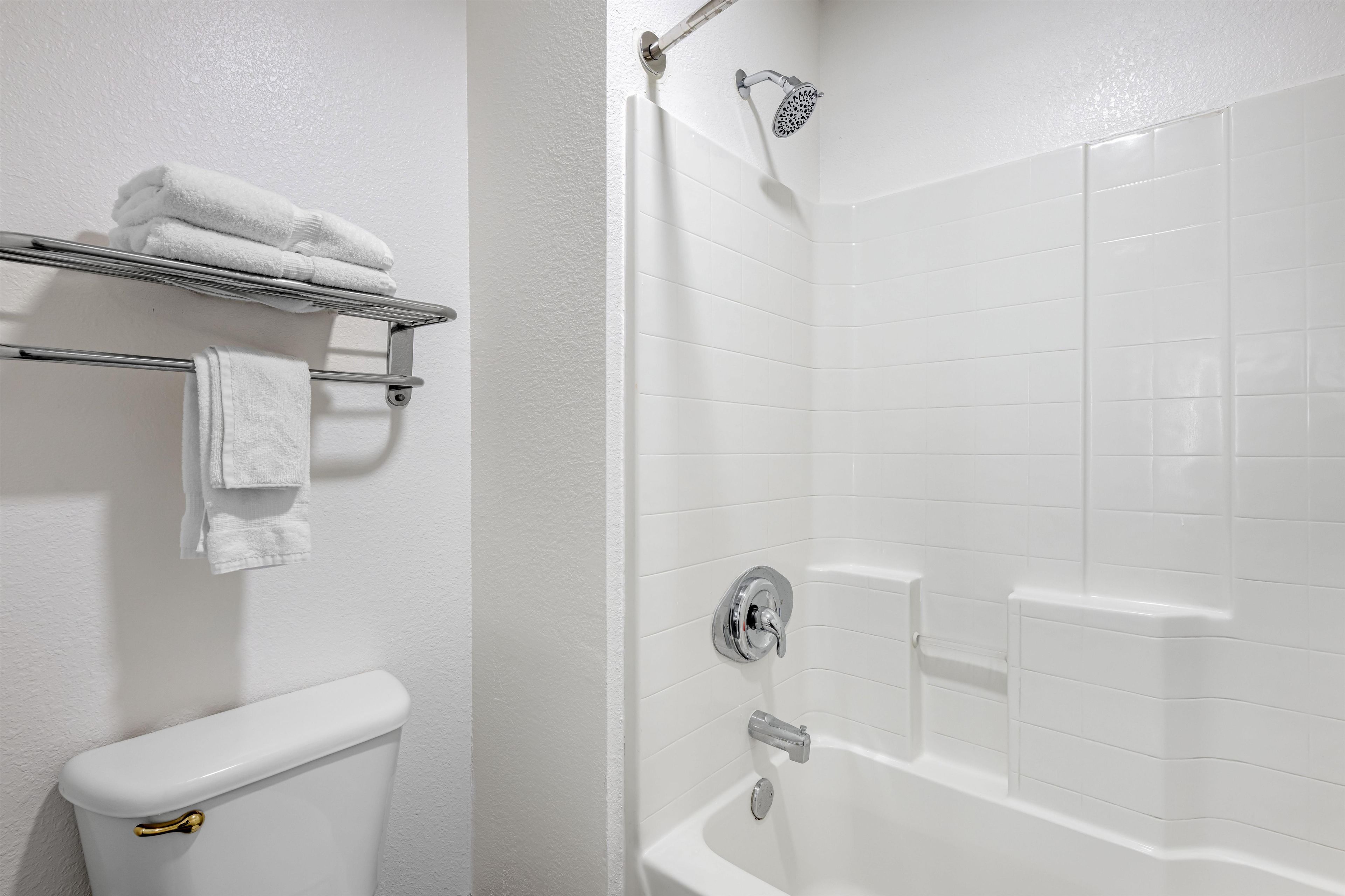 Un baño con inodoro, un perchero con toallas dobladas, una ducha con cabezal de ducha de mano y una bañera con grifo.