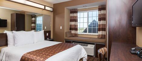 A hotel room with a bed, a desk, a chair, a window with curtains, a television, and a mirror.