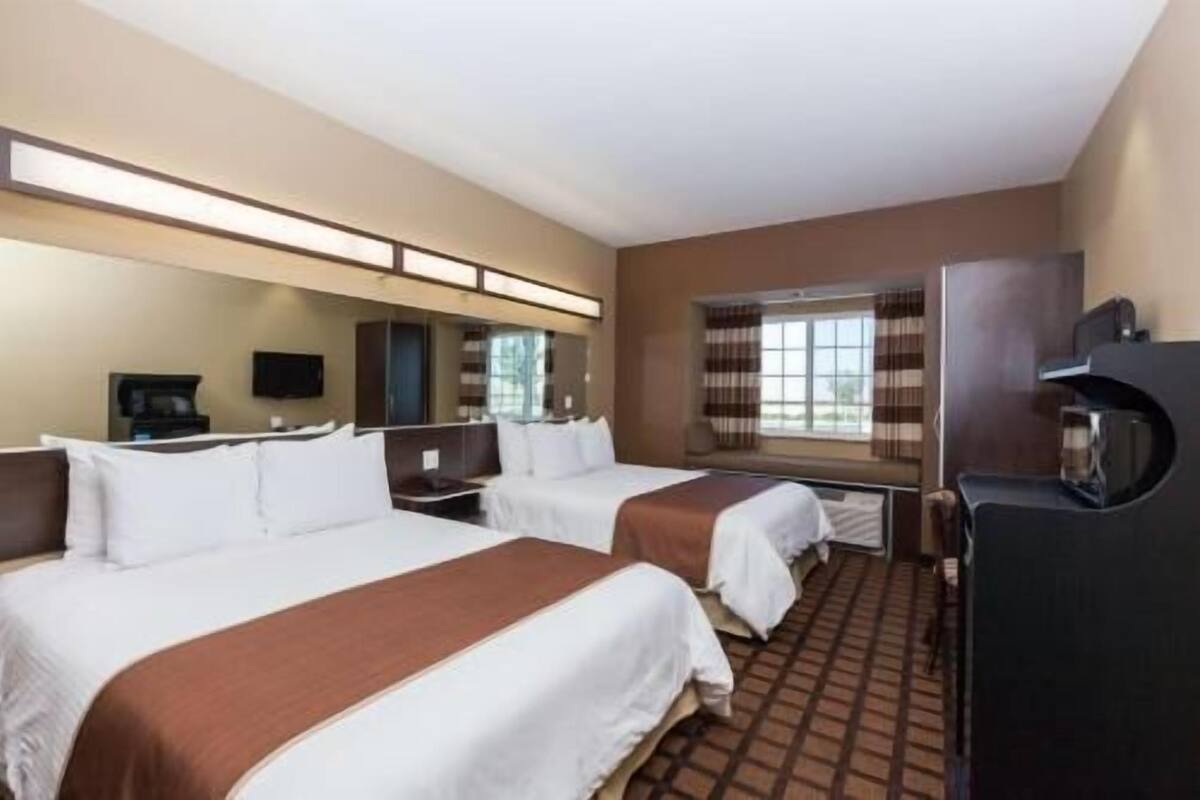 A hotel room with two beds, a large mirror, a television, and a refrigerator.