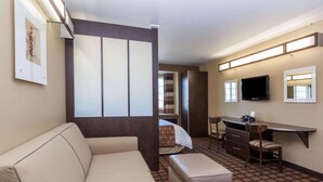A hotel room with a sofa, a desk with chairs, a TV, and a bed. - Microtel Inn & Suites by Wyndham Wheeler Ridge (Arvin)