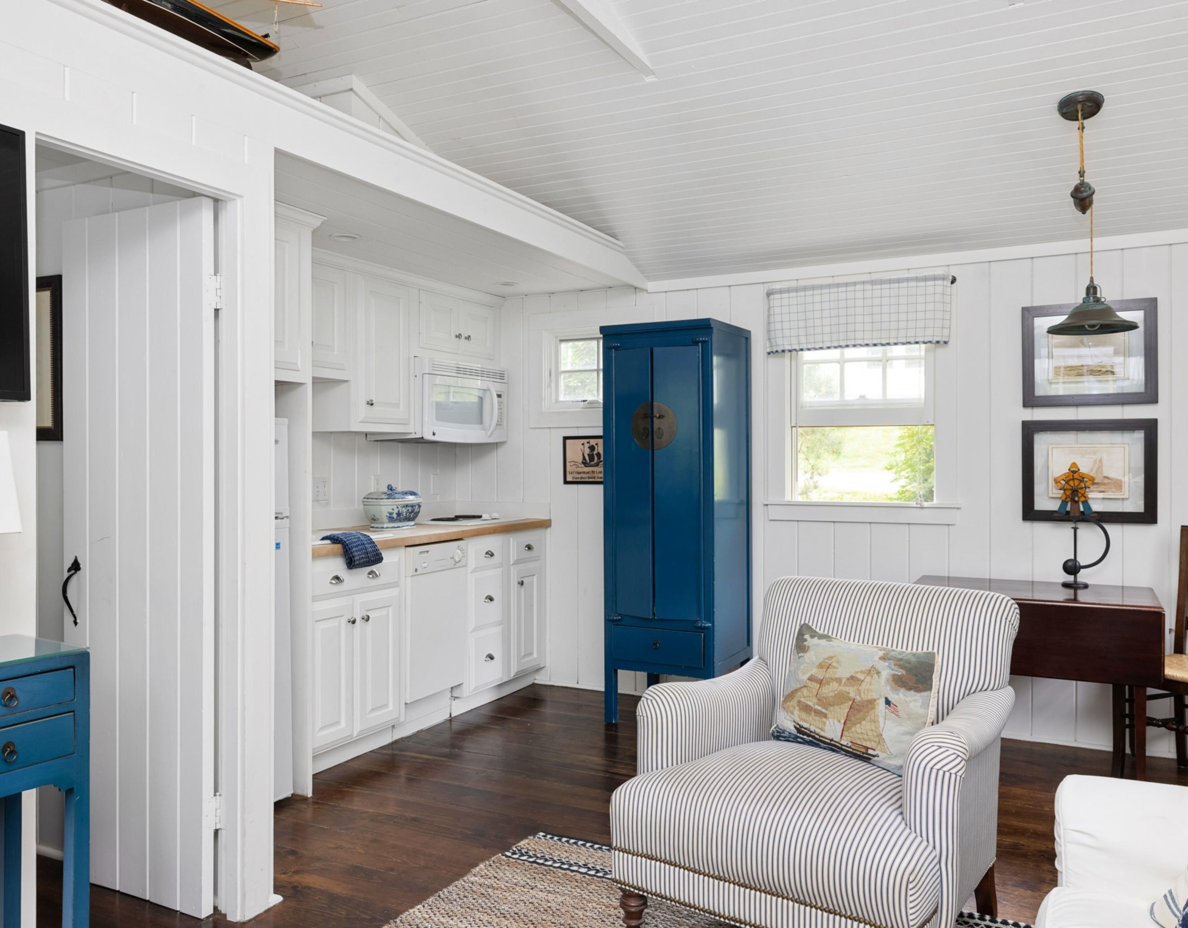 A room with white cabinetry, a blue cabinet, a striped armchair, and a wooden floor.