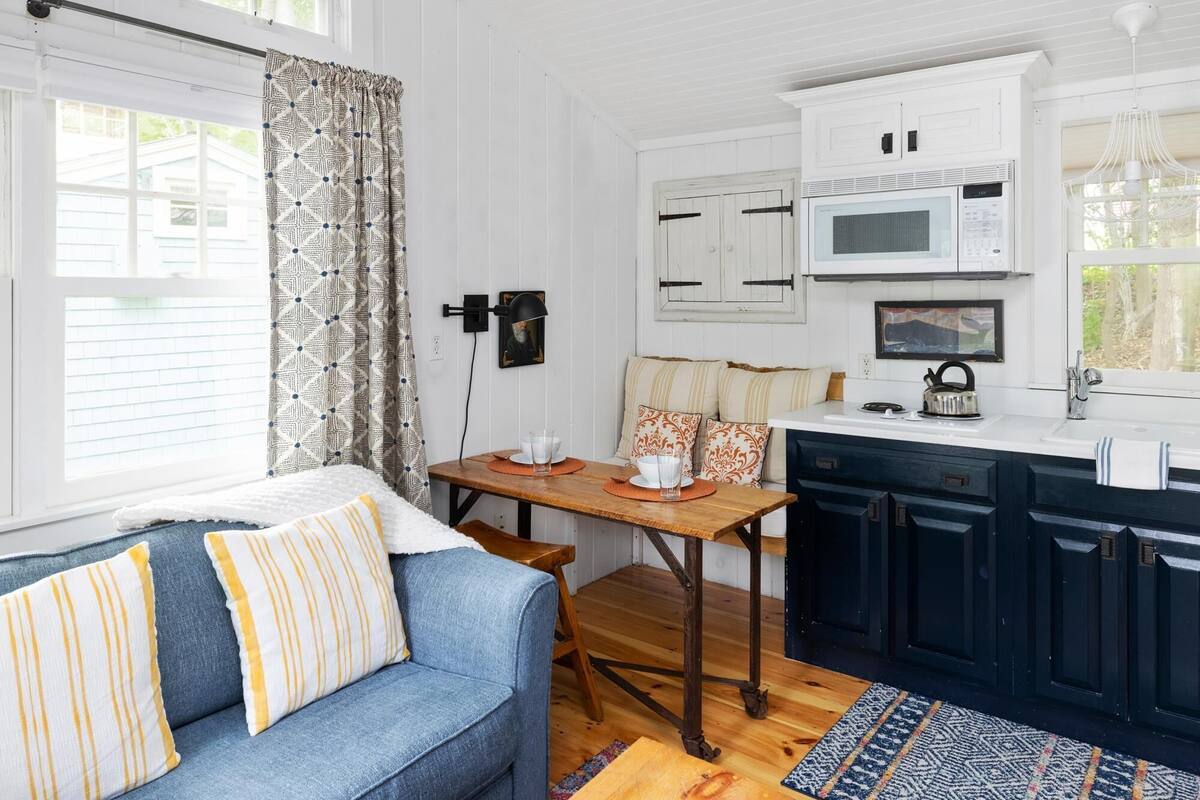 Ett mysigt rum med en blå soffa, ett matbord i trä, vita väggar och en köksdel med mörka skåp och en mikrovågsugn.