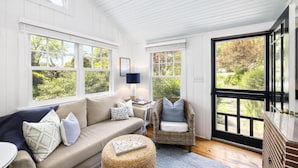 A cozy room with a sofa, a wicker chair, and a large window. - The Cottages at Cabot Cove (Kennebunkport)