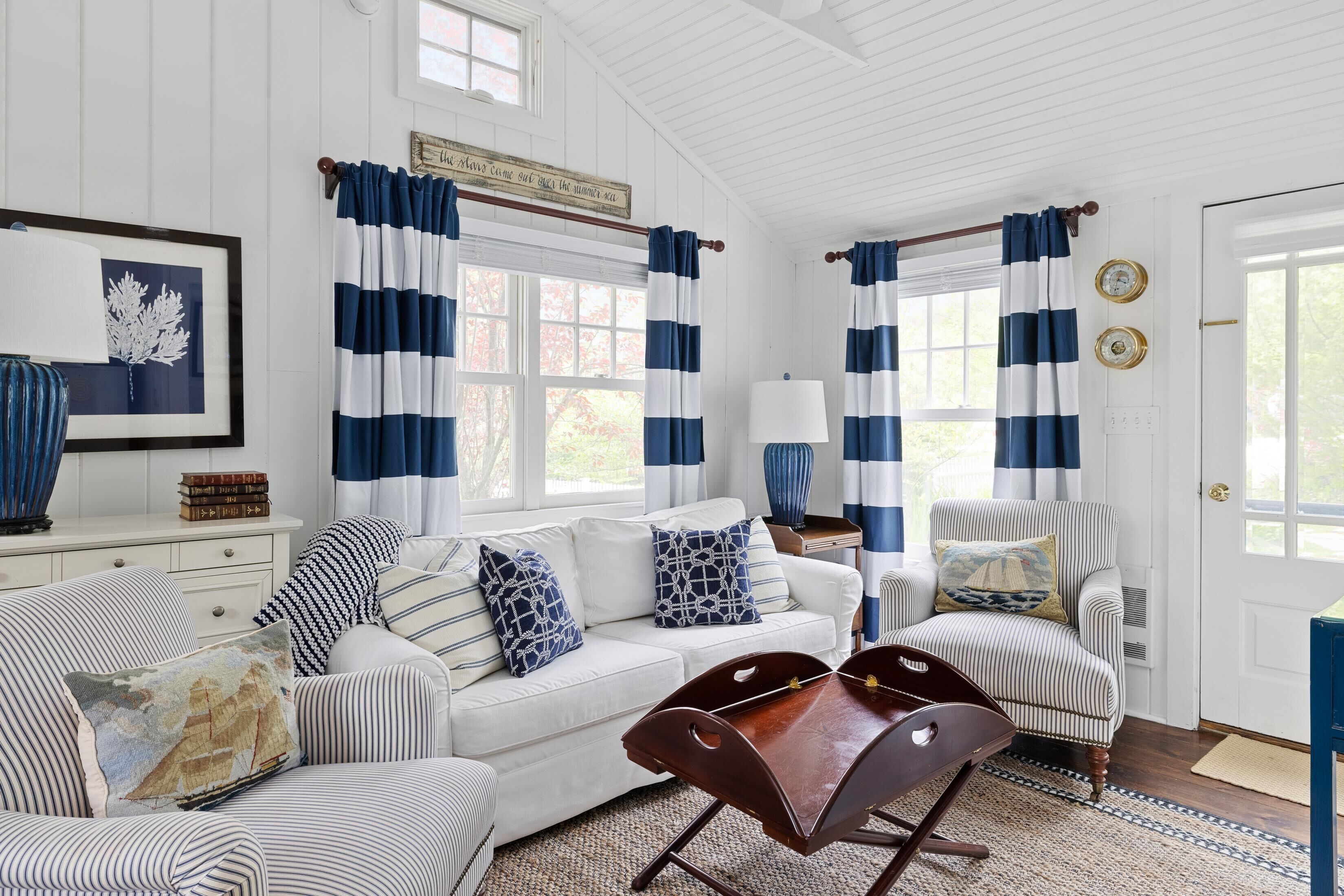 A white room with striped curtains, a sofa, a chair, and a wooden table.