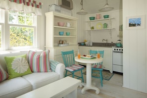A bright kitchen with white cabinetry, a dining table, chairs, and a window with a view of trees.